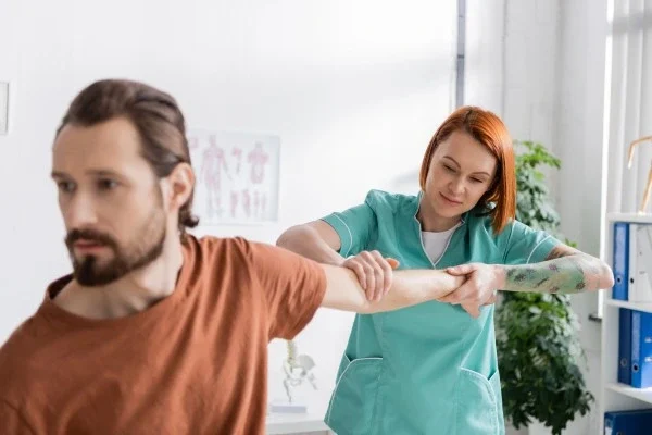 redhead-physiotherapist-stretching-arm-of-blurred-2026-03-20-03-48-13-utc (1)